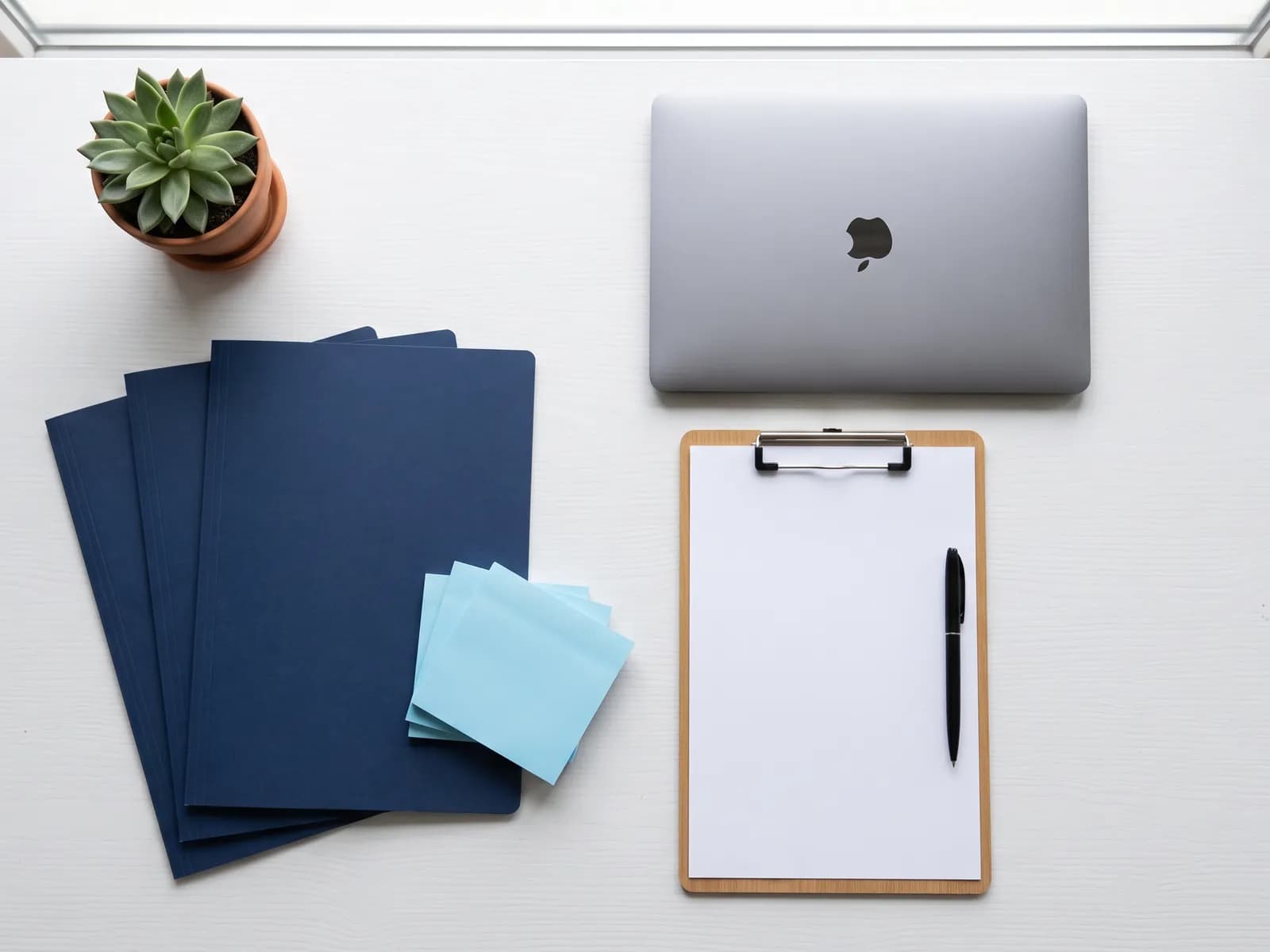Tidy desk from above with a closed laptop, blank folders and a clipboard