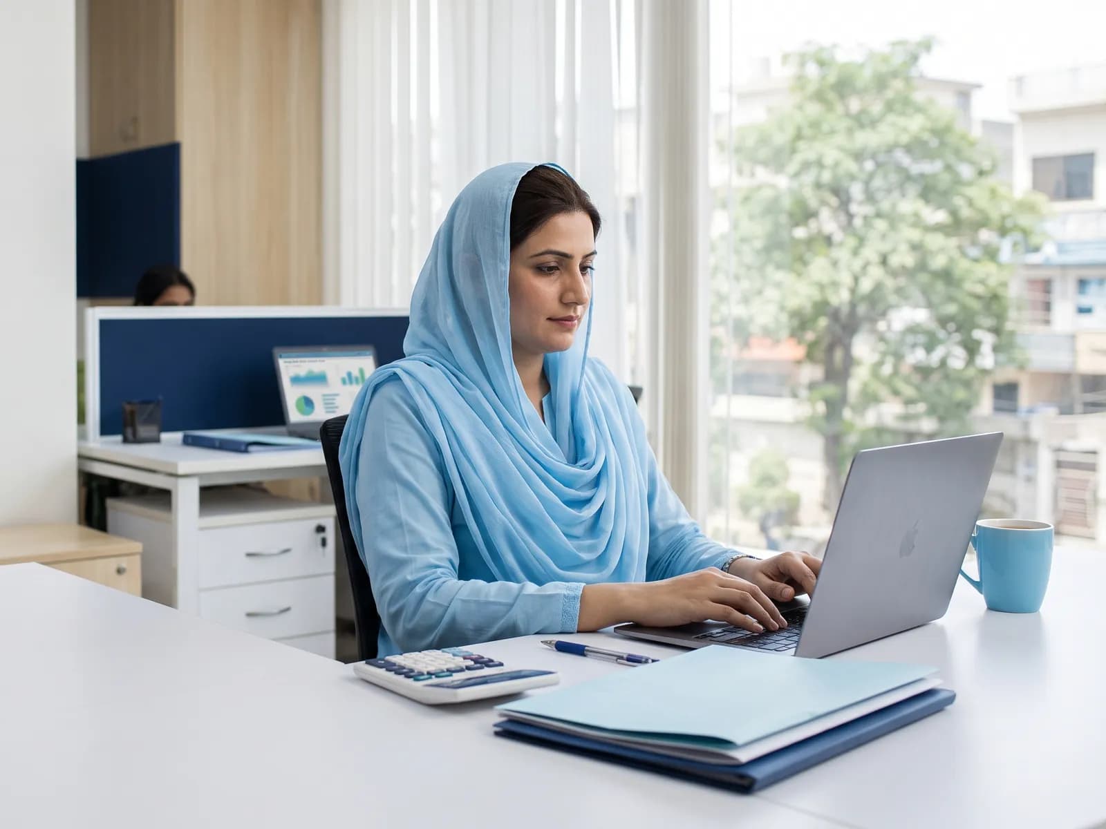 Medical biller in a light blue dupatta working on claims at a laptop in the office