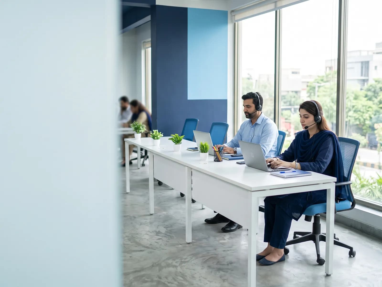 Transcriptionists with headsets typing at a long desk in a bright office